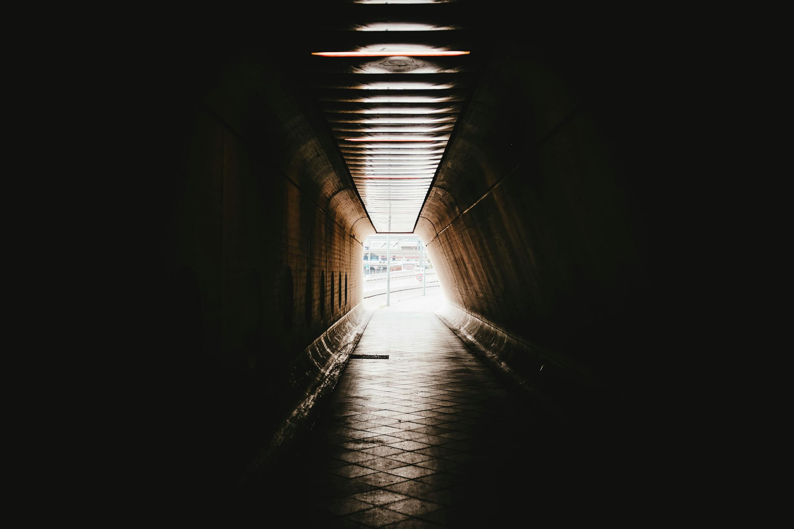 A dark and mysterious tunnel leading to a brightly lit street, creating a dramatic contrast.