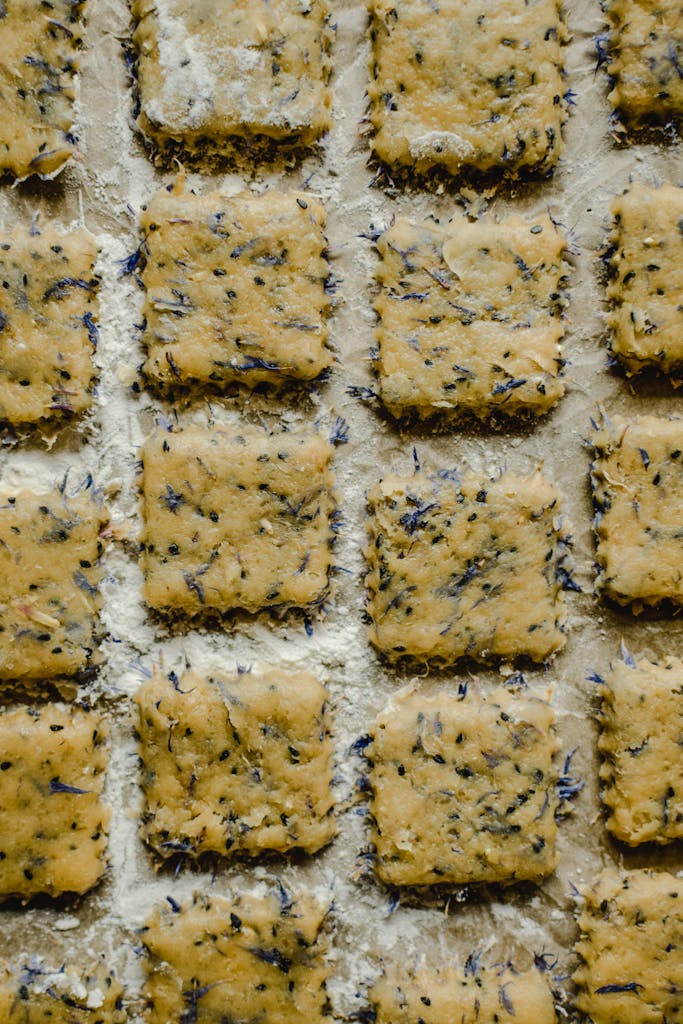 Close-up of homemade herbal square crackers arranged on a floured surface, ready for baking.